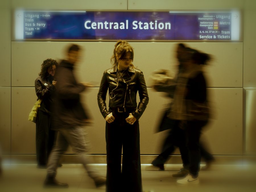 Maya Vero – Whispers: a woman stands still at Centraal Station while commuters blur past