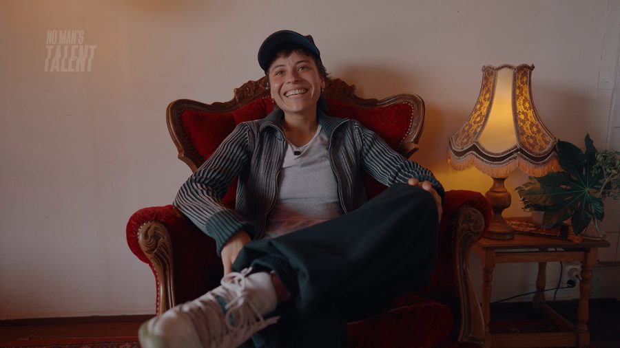 No Man’s Talent: a smiling person in a red armchair beside a lamp